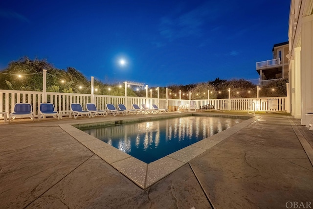 pool at night with a fenced in pool, a patio area, and fence