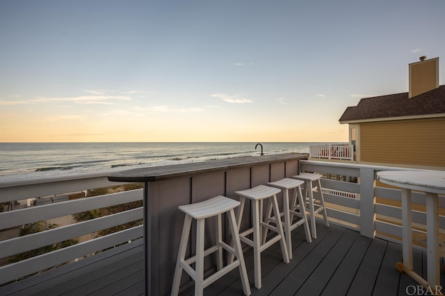 deck at dusk with a water view, a beach view, and outdoor dry bar