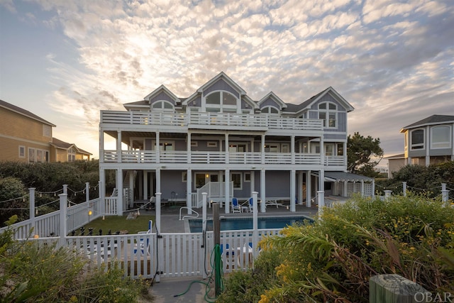 rear view of house with a balcony, fence private yard, a community pool, and a gate