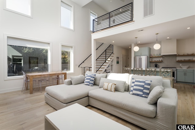 living area featuring visible vents, baseboards, a towering ceiling, light wood-style floors, and stairway