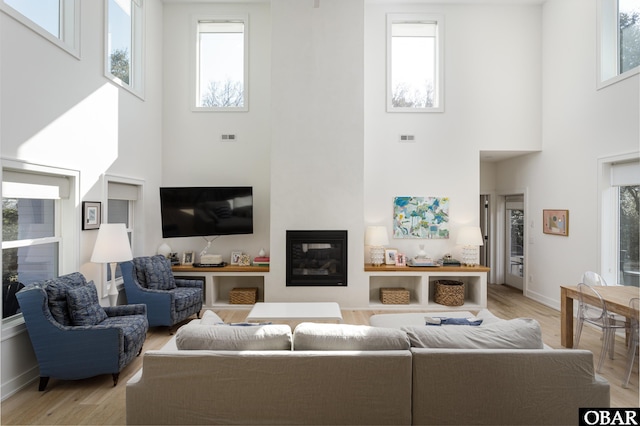 living room with light wood-type flooring, a glass covered fireplace, visible vents, and baseboards