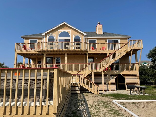 back of house featuring a shingled roof, a deck, a chimney, and stairs