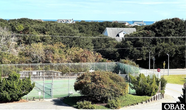 view of tennis court featuring a view of trees and fence
