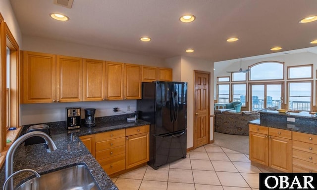 kitchen with dark stone countertops, open floor plan, a sink, and freestanding refrigerator