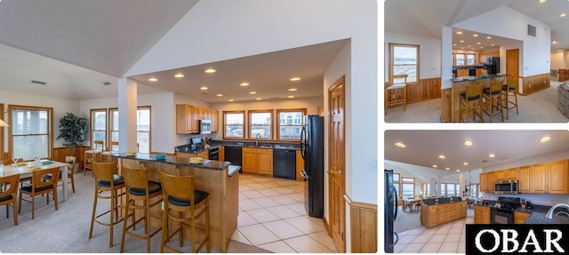 kitchen with a peninsula, black appliances, a breakfast bar area, and a wainscoted wall