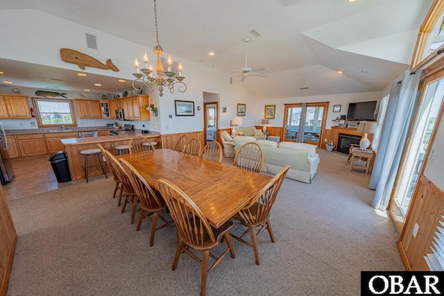 dining space featuring a glass covered fireplace, vaulted ceiling, light colored carpet, and a wainscoted wall