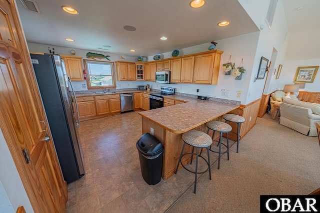 kitchen featuring visible vents, a breakfast bar, a sink, appliances with stainless steel finishes, and a peninsula