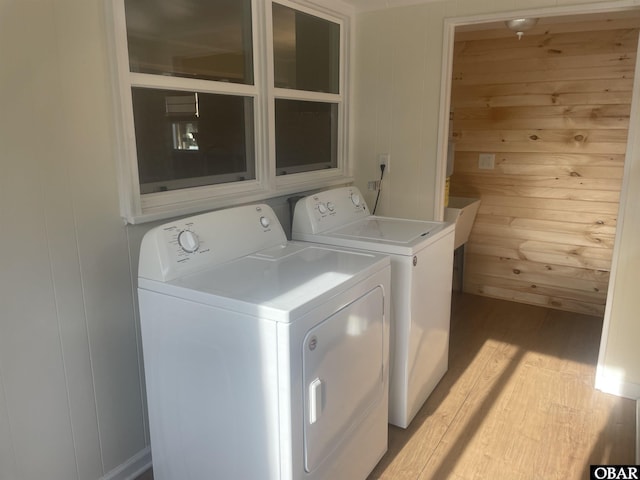 washroom featuring laundry area, separate washer and dryer, light wood-style flooring, and wooden walls