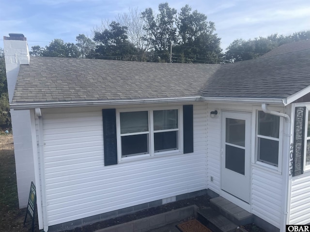 view of property exterior featuring entry steps, roof with shingles, and a chimney