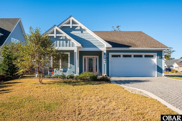 view of front of property featuring a garage, covered porch, decorative driveway, board and batten siding, and a front yard