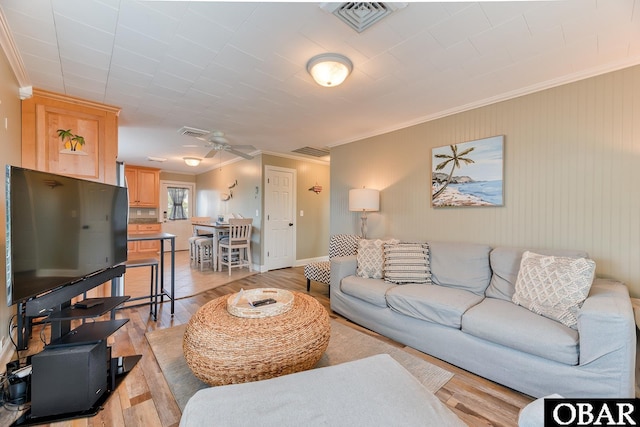 living room featuring crown molding, light wood-style flooring, baseboards, and visible vents