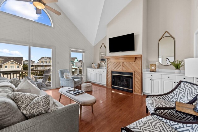 living area with dark wood finished floors, a tiled fireplace, ceiling fan, a residential view, and high vaulted ceiling