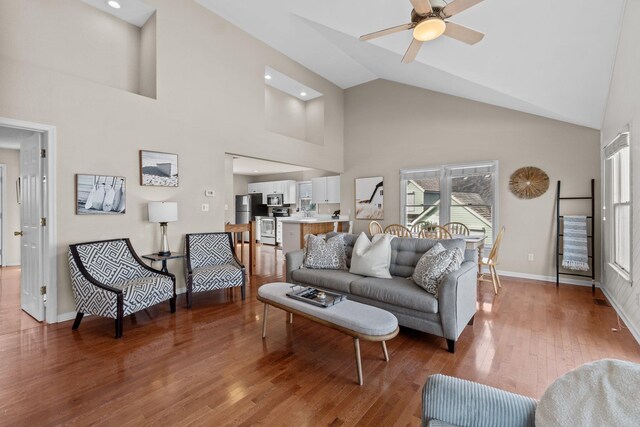 living room with ceiling fan, high vaulted ceiling, wood finished floors, and baseboards