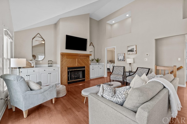 living area with baseboards, wood finished floors, a fireplace, high vaulted ceiling, and recessed lighting