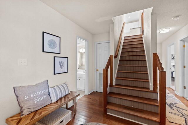 stairs with visible vents, a textured ceiling, baseboards, and wood finished floors