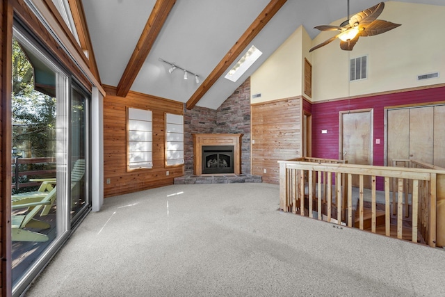 unfurnished living room featuring a stone fireplace, wooden walls, carpet flooring, visible vents, and beamed ceiling