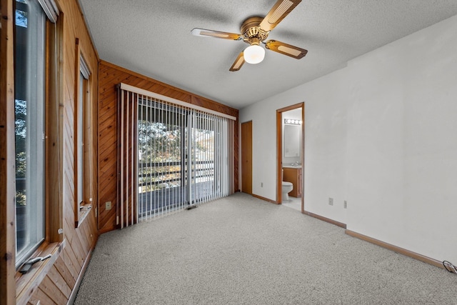 empty room featuring wood walls, ceiling fan, a textured ceiling, and light colored carpet