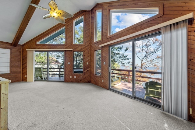 unfurnished living room featuring carpet floors, beam ceiling, high vaulted ceiling, and wooden walls