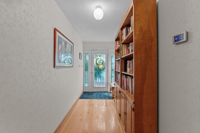 entryway with a textured ceiling, a textured wall, light wood-type flooring, and baseboards