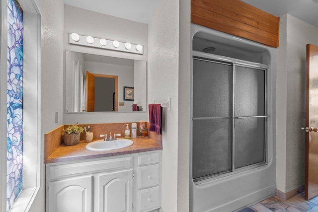 bathroom with combined bath / shower with glass door, a textured wall, and vanity