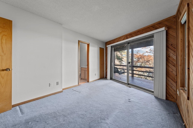 empty room featuring wooden walls, baseboards, a textured ceiling, and light colored carpet