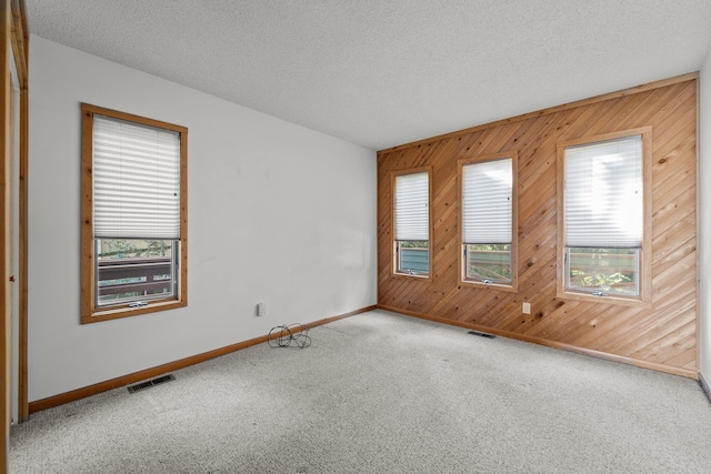 empty room featuring carpet floors, visible vents, a textured ceiling, and wooden walls