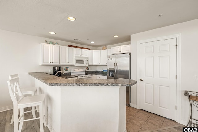 1700 Paget Rd Unit B3, Kill Devil Hills, NC 27948 - kitchen featuring white appliances, a peninsula, white cabinets, recessed lighting, and a breakfast bar area