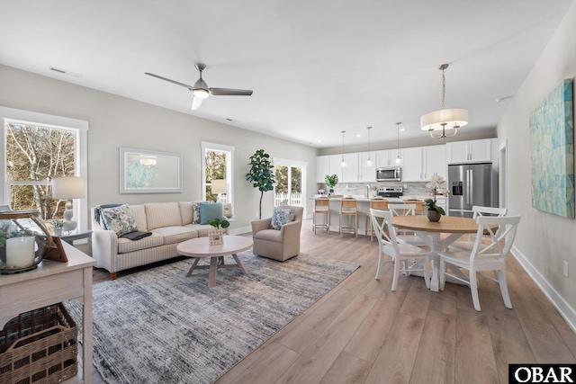 living room featuring light wood-type flooring, visible vents, baseboards, and ceiling fan