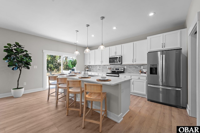 kitchen with stainless steel appliances, decorative backsplash, light countertops, white cabinetry, and light wood-type flooring