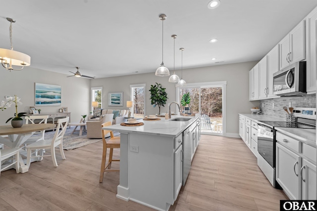 kitchen featuring a center island with sink, a sink, stainless steel appliances, light wood-type flooring, and backsplash