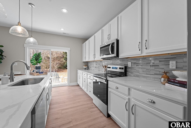 kitchen with a sink, backsplash, light wood-style floors, appliances with stainless steel finishes, and white cabinets