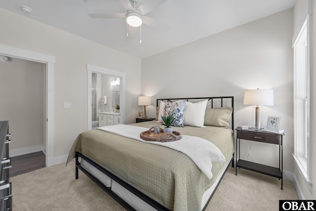 bedroom featuring light colored carpet, ensuite bath, baseboards, and ceiling fan