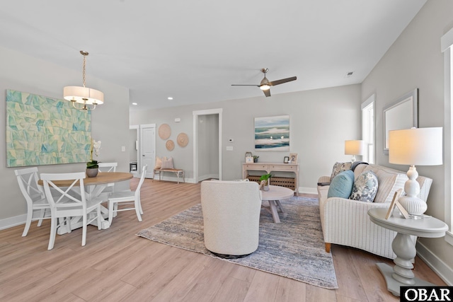 living area with visible vents, baseboards, light wood-style flooring, and ceiling fan with notable chandelier