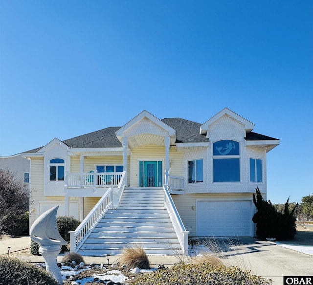 raised beach house with a porch, a garage, driveway, stairway, and roof with shingles