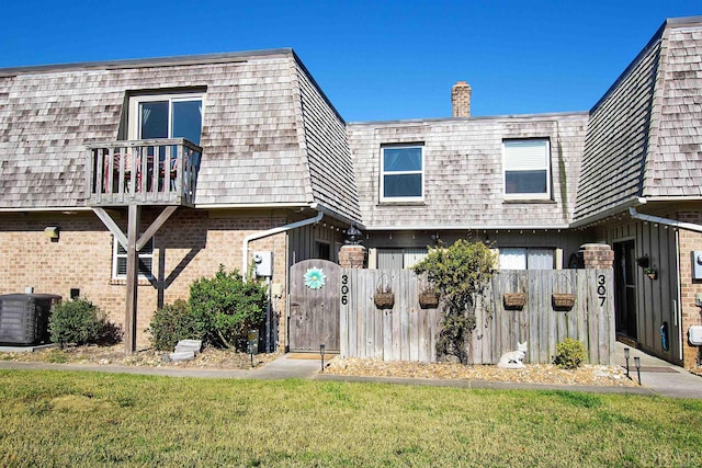 view of property with brick siding, mansard roof, a gate, central AC, and a balcony