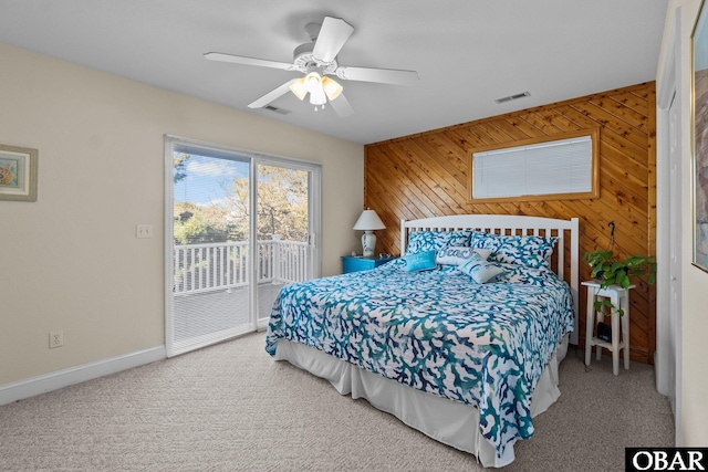 carpeted bedroom featuring access to exterior, visible vents, wood walls, and ceiling fan