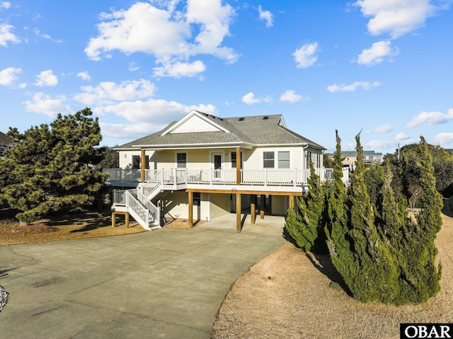 raised beach house with driveway, a shingled roof, and a porch