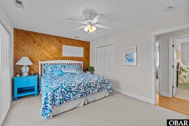 carpeted bedroom with a closet, visible vents, a ceiling fan, wooden walls, and baseboards