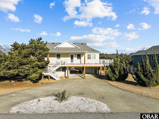 coastal home with a porch, a shingled roof, a carport, driveway, and stairs