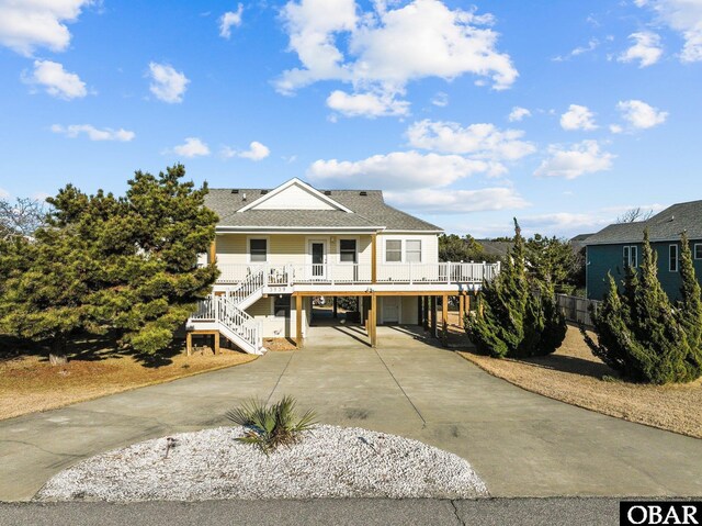 coastal home with a porch, a shingled roof, a carport, driveway, and stairs