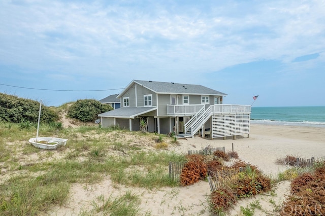 rear view of property with stairs, a deck with water view, and a view of the beach