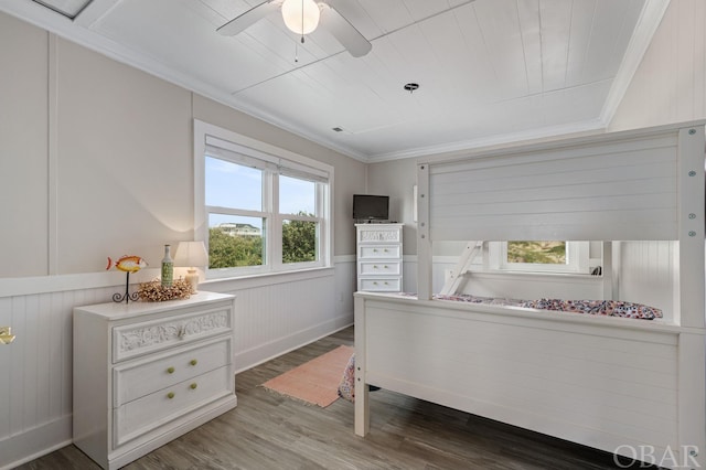 bedroom featuring dark wood-style floors, a wainscoted wall, crown molding, visible vents, and a ceiling fan