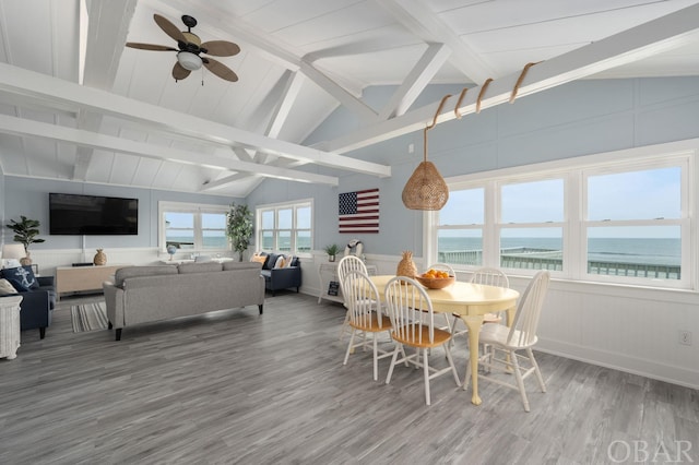 dining room with a water view, vaulted ceiling with beams, and wood finished floors