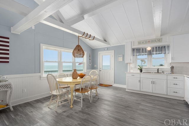 dining area with baseboards, wainscoting, lofted ceiling with beams, dark wood-type flooring, and a water view