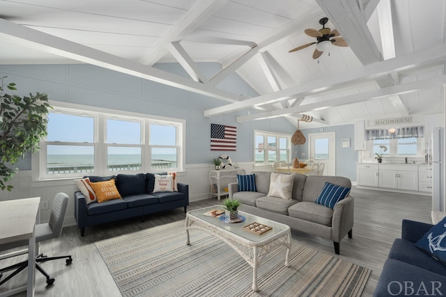 living area featuring a water view, lofted ceiling with beams, wood finished floors, and wainscoting