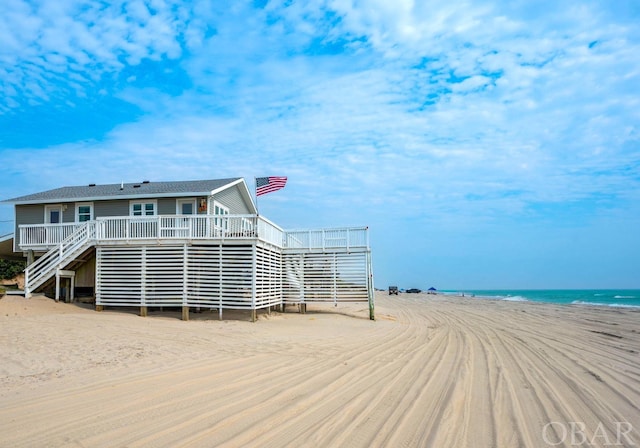 exterior space featuring stairway, a deck with water view, and a beach view