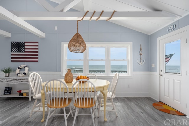 dining area with a wainscoted wall, a water view, wood finished floors, and vaulted ceiling with beams