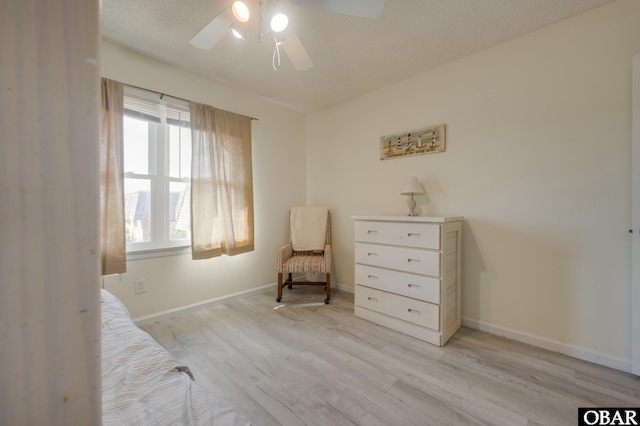 sitting room featuring a textured ceiling, light wood finished floors, a ceiling fan, and baseboards