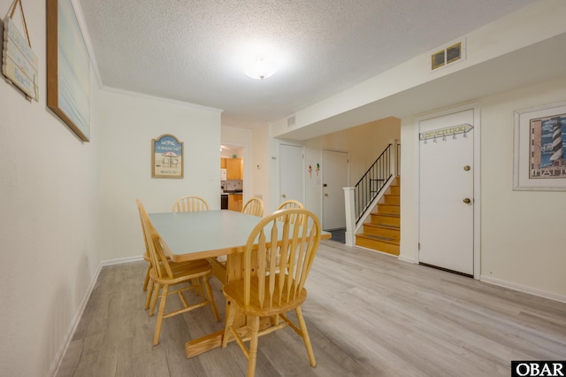 dining room featuring light wood-type flooring, visible vents, a textured ceiling, and stairs