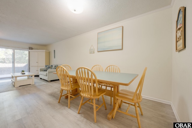 dining space featuring baseboards, light wood-style floors, a textured ceiling, and crown molding